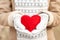 Girl hands in white knitted mittens holding romantic red heart