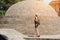 Girl in a hat and with a backpack standing near a brick dome. Sunny day