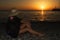 A girl in a hat with beautiful slender long legs watching the sunset on the sea.