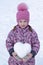 Girl in hat, coat and mittens holding a snowball in the shape of a heart.