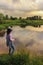 Girl in a hat fishing rod on the lake, summer landscape, storm clouds in the sky. outdoor activities. rear view