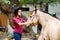 The girl in the hat holds the horse by the buckle. Outside.