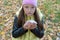 The girl in the hat and jacket sneezes and wipes her nose with a napkin in the autumn forest while walking.  Flu season and cold