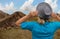 Girl in hat looks at mountain terrain and thick clouds and blue sky from a cliff. White middle aged woman stays back to us and