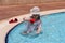 Girl in a hat in the pool playing with a bucket