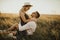 A girl in hat sits in hands guy on ground in middle of tall grass in meadow