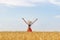 Girl in hat stands in middle of wheat field raising his hands to sky