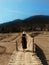 A Girl in the hat walking to bamboo bridge in rice fields on the background of the mountain