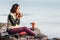 Girl is having breakfast and drinking coffee on a cliff top with a view of sunrise in mountains, and a thick fog is creeping