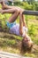 Girl having fun in park hanging upside down on green rural countryside.