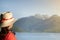 Girl with headphones and stalk hat and red dress on looking a the mountains by a lake