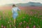 A girl with her back to the camera in a field of pink flowers, at the bottom of a high mountain