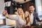 Girl and her beautiful parents are cutting vegetables and smiling while cooking in kitchen at home make selfie