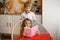 Girl with her hair in red dress is reading pink book sitting in wicker chair. Her brother looks over her shoulder