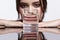 Girl hides her face behind a glass with water. Optical distortion portrait of young woman at the mirror table
