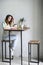 A girl at a high table sits with coffee, head bent over a white brick wall.