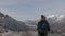 A girl with a hiking backpack walks along the road in the winter mountains of the Alps