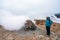 Girl with hiking gear infront of sulphur steam vents in Iceland during heavy cold wind. Mineral rich and textured ground infront.