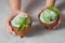 A girl hold two halves of coconut with green mint sorbet with sprig of mint and coconut chips on a gray concrete.