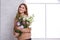 A girl is holding a bouquet of Japanese roses against a white window