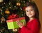 Girl Holding Christmas Present In Front Of Tree