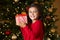 Girl Holding Christmas Present In Front Of Tree