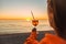 Girl Holding Glass of Drink on Beach at Beautyfull Romantic Sunset. Glass and Hand Close Up. View From Back