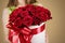 Girl holding in hand rich gift bouquet of 21 red roses. Composition of flowers in a white hatbox. Tied with wide red ribbon and b