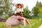 Girl holding a large bouquet of peonies. Young teenager in a hat with wide brim is sitting in a flowering meadow.