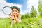 Girl holding magnifier lays alone on green grass