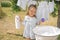 Girl holds bottle of liquid laundry detergent in hands, standing at basin for hand washing clothes.