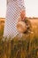 A girl holds a hat and flowers in her hand walking in a wheat field