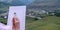 A girl holds in her hand a paintbrush near a white canvas on the background of a mountain settlement on a summer evening