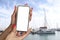 Girl holds in his hand a smartphone close-up, with a white screen against the backdrop of the sea and yachts. Mock-up Technology