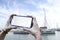 Girl holds in his hand a smartphone close-up, with a white screen against the backdrop of the sea and yachts. Mock-up Technology