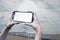 Girl holds in his hand a smartphone close-up, with a white screen on a background of sea. Mock-up Technology