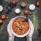 Girl holds a plate of tomato soup in her hands, surrounded by ingredients for cooking, tomatoes, garlic, herbs seasonings, on