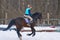 A girl on a horse jumps gallops. A girl trains riding a horse in a small paddock. A cloudy winter day