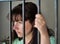 The girl is imprisoned in jail, behind bars. Deprivation of liberty