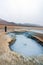 Girl infront of bubbling hot mud pool with mountains and s-shaped road in the background in the Hverarond volcanic area in Iceland