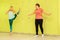 A girl with an instructor performs an exercise near a yellow wall with ropes in the gym.