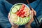 Girl in jeans holding vegan watermelon poke bowl with avocado, cucumber, mung bean sprouts and pickled ginger. Top view, overhead.