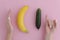 Girl jokingly measures the size of a banana and cucumber comparing with the man long or large size. On pink