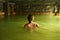 Girl kid child bathe swim in outdoor cave, dirty hot springs. Thermal water bath pool. Healthy natural clay. Yellow