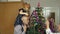 Girl kid with senior grandma, grandpa decorating artificial Christmas tree with ornaments and toys