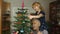 Girl kid with senior grandpa decorating artificial Christmas tree with ornaments and toys at home