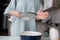 A girl in the kitchen sows flour through a metal sieve into a ceramic beating bowl. The concept of baking at home. The