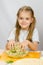 Girl at kitchen table with a slight smile mixes hands in a bowl the grated cheese with herbs