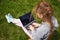 Girl with laptop on green grass. Remote schooling. The child works at the computer