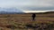 Girl with large backpacks and trekking poles walks past the Tolbachik volcano.